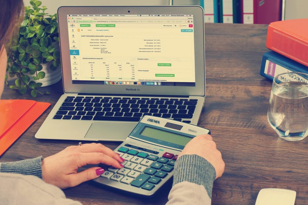 A woman calculating financial expenses on a calculator next to an open laptop.