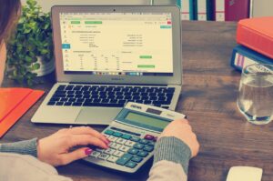 A woman calculating financial expenses on a calculator next to an open laptop.