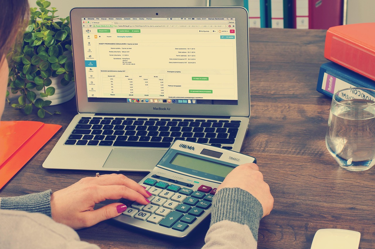 A woman calculating financial expenses on a calculator next to an open laptop.