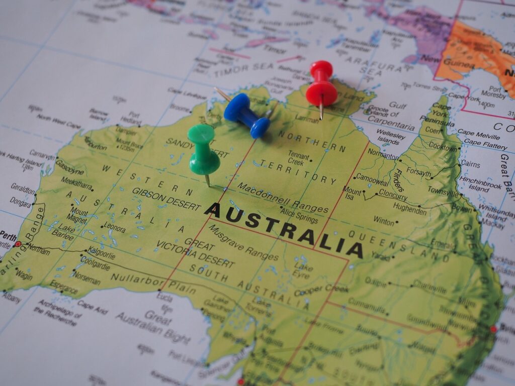 A printed map of Australia with colorful pushpins placed on different regions.