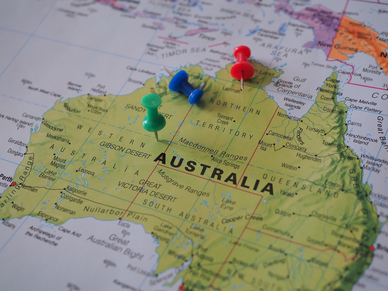 A printed map of Australia with colorful pushpins placed on different regions.
